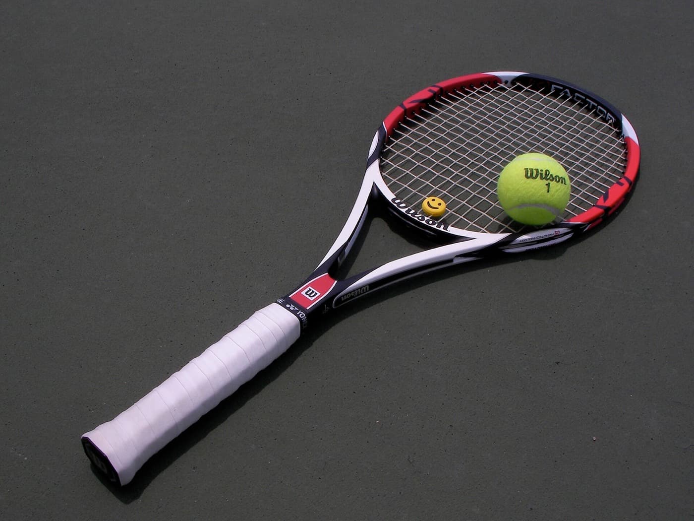 Tennis racket beside a tennis ball on a court surface.