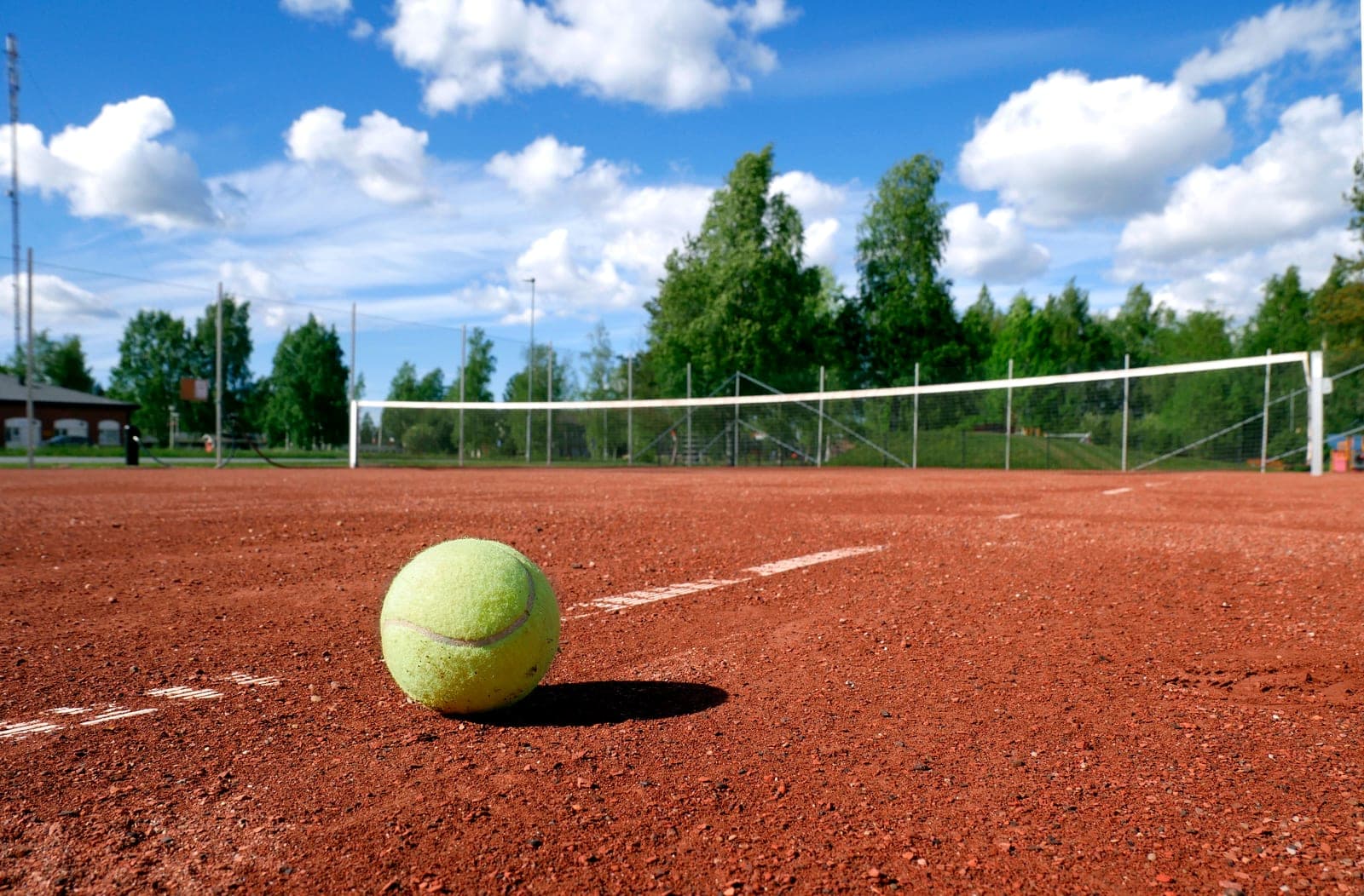 A tennis ball rests on the clay of a tennis court.