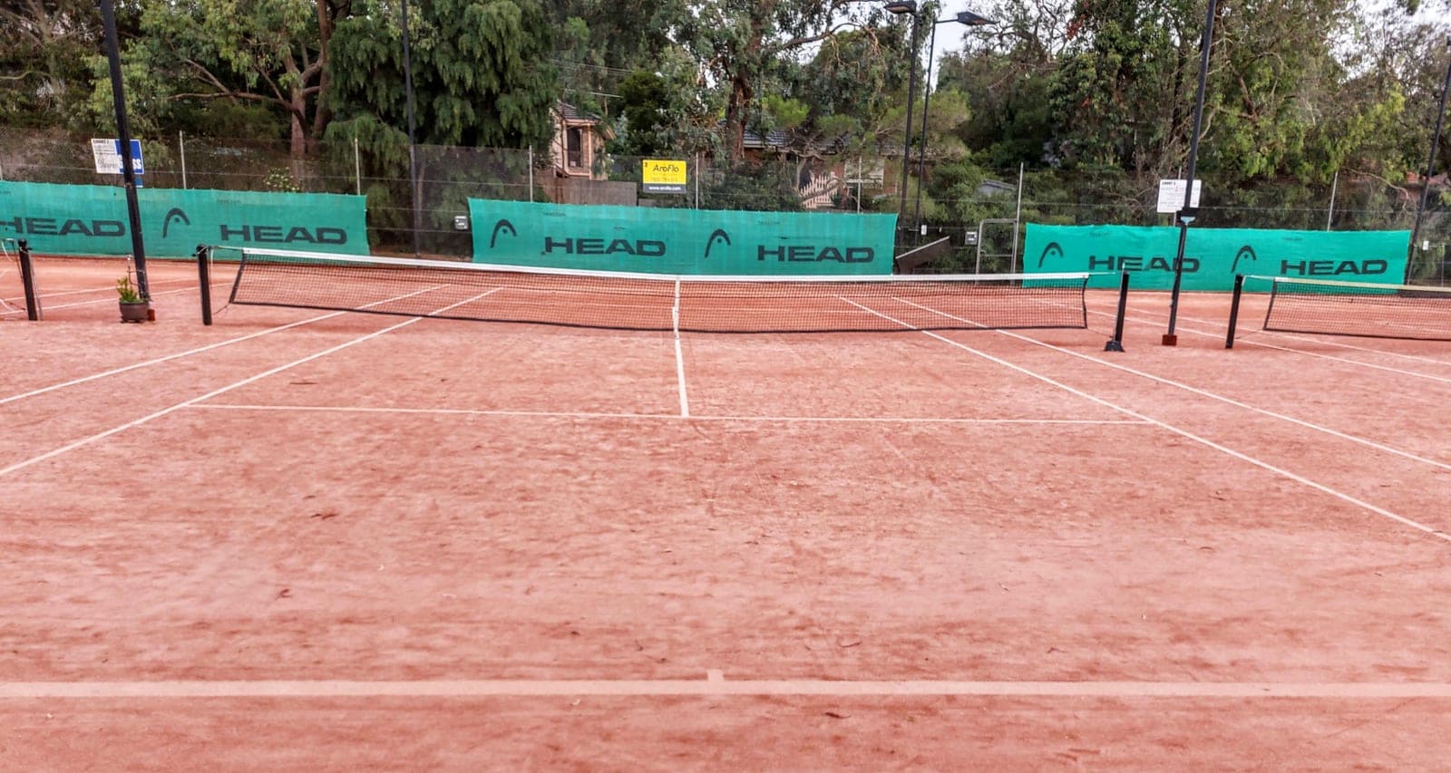 An empty clay tennis court with the net in the foreground.