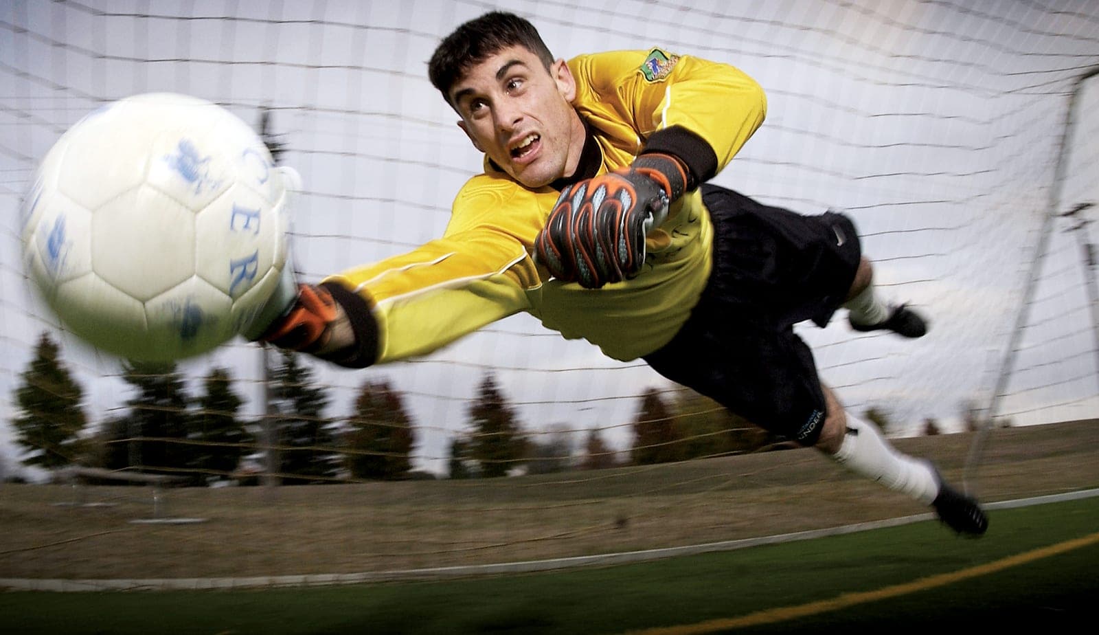 A goalkeeper dives to make a save as the ball flies toward the goal.