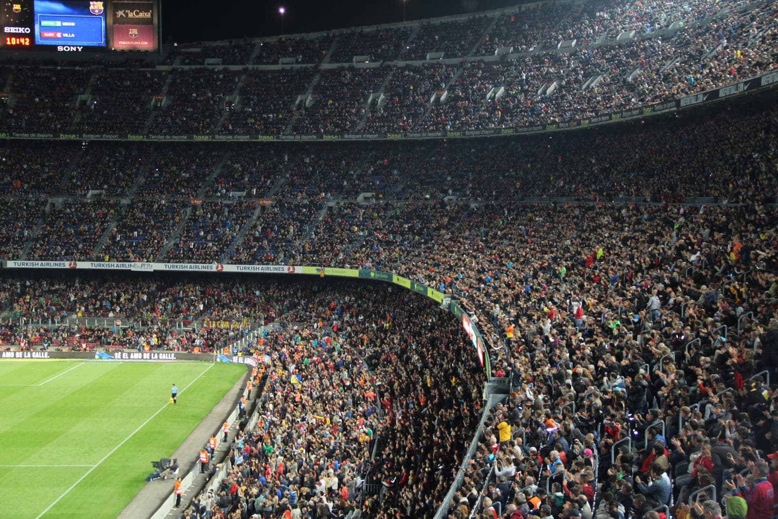 A packed football stadium with the pitch below and supporters filling the stands.
