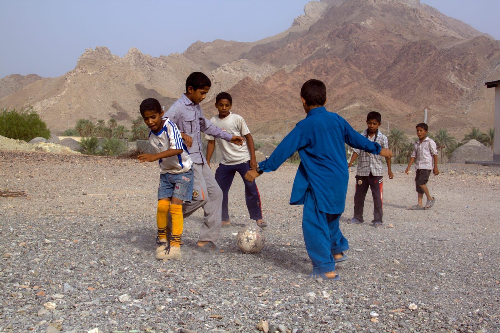 Children play football together on a dusty pitch, contesting the ball.