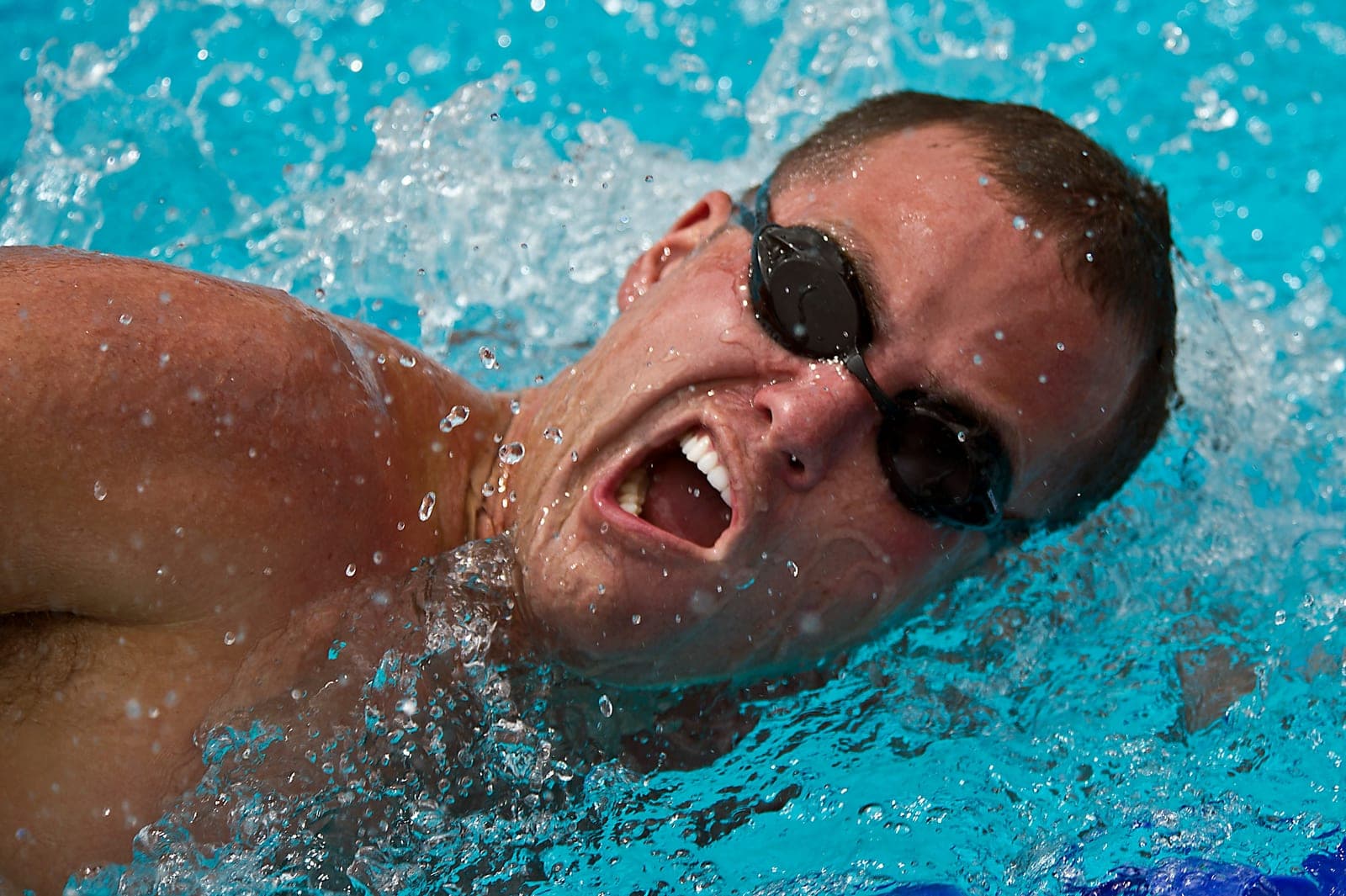 A close-up of a swimmer mid-stroke, water spraying, breathing to the side.