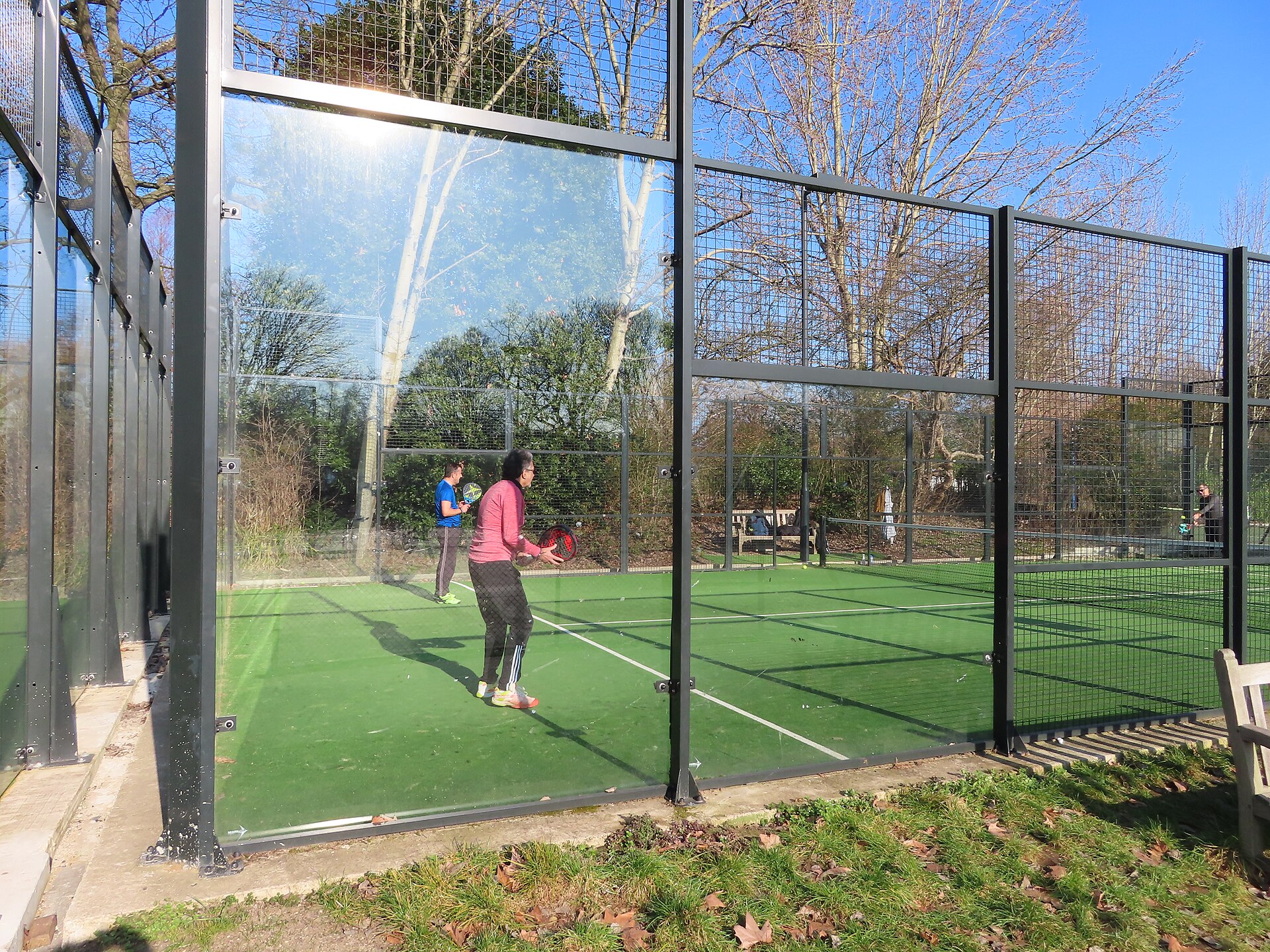An enclosed padel court with glass back walls and metal mesh sides, viewed from outside the enclosure.